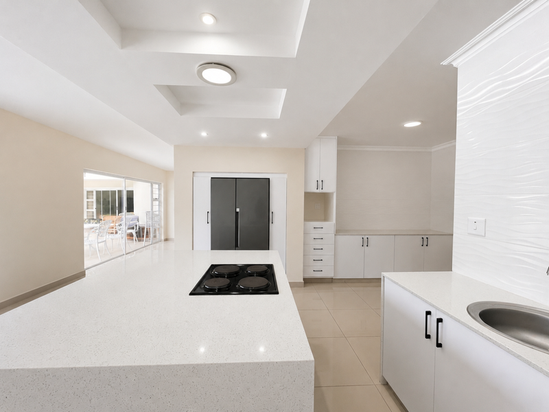 Modern kitchen featuring a large central island with a built-in hob, quartz countertops, ample white cabinetry, and sleek tiled flooring.