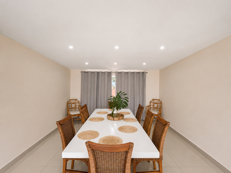 A bright and well-maintained dining room featuring neutral walls, tiled flooring, and recessed downlighting, providing a clean and functional space for meals.