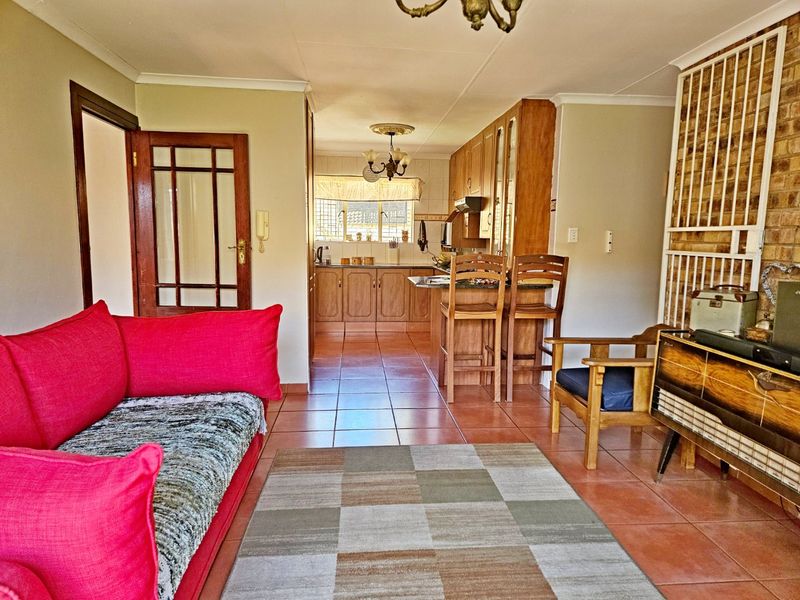 Open-plan living and kitchen area featuring tiled floors, wooden cabinetry, a breakfast bar, and an exposed brick feature wall with a security gate.