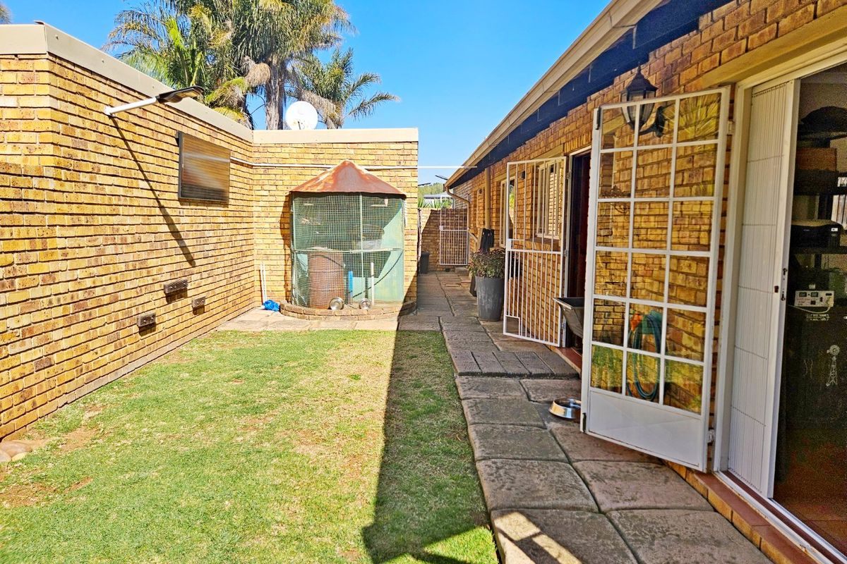 A private rear courtyard featuring a brick-walled garden, paved walkway, and direct access to the interior through a glass-paned security door.