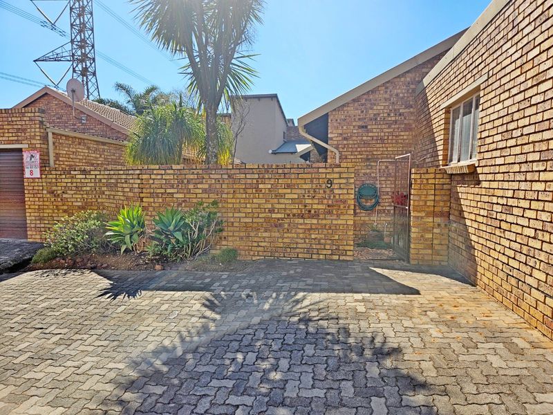 Front exterior view of the townhouse featuring a face brick facade, paved driveway, and secure gated entrance.