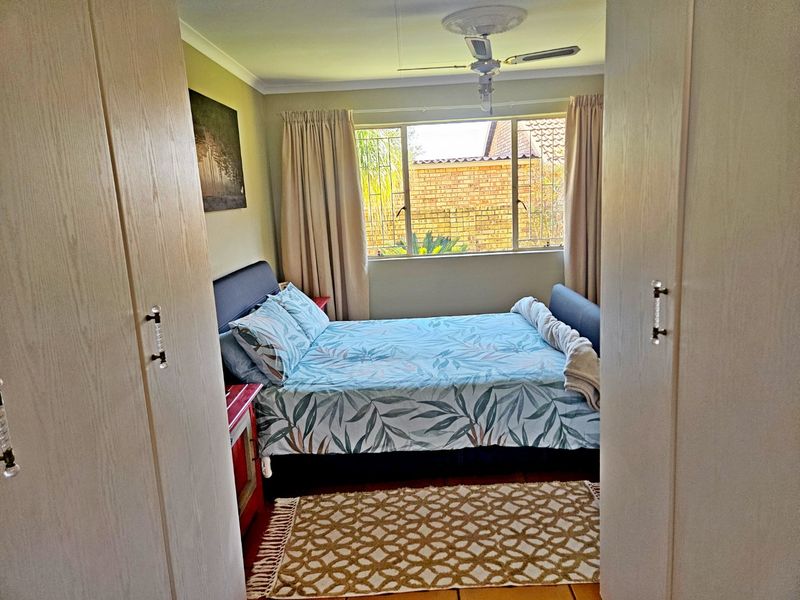 A bedroom featuring built-in cupboards, a ceiling fan, and natural light from a window overlooking the exterior.