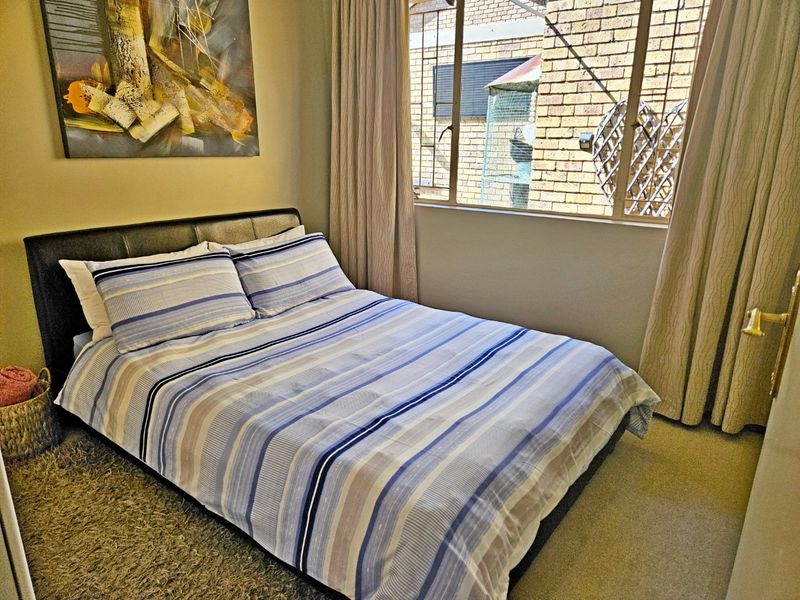 A cozy bedroom featuring carpeted flooring and a window with views of the exterior brickwork.