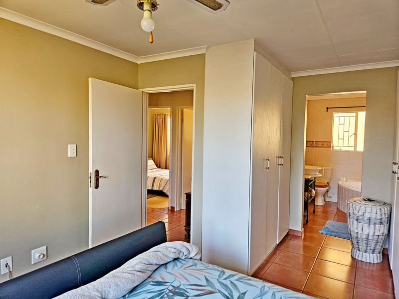 A bedroom featuring built-in cupboards, tiled flooring, a ceiling fan, and direct access to an en-suite bathroom.