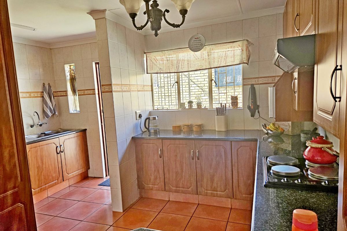 A functional kitchen featuring wooden cabinetry, granite countertops, a built-in hob with extractor fan, and tiled flooring with a separate scullery area.