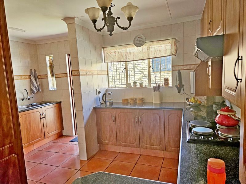 A functional kitchen featuring wooden cabinetry, granite countertops, a built-in hob with extractor fan, and tiled flooring with a separate scullery area.