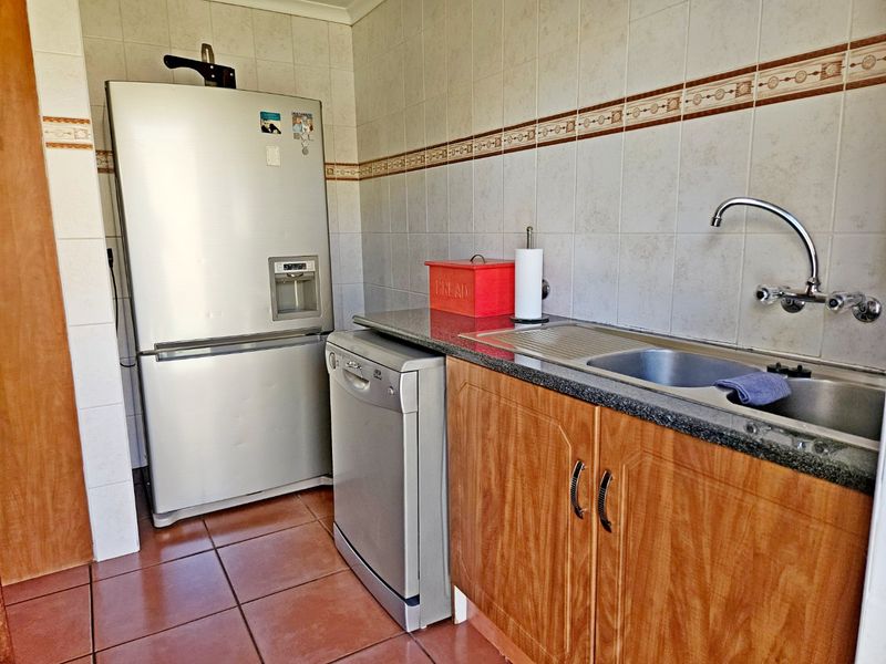 A functional scullery area featuring tiled splashbacks, granite countertops, stainless steel sink, and wood-look cabinetry, providing additional prep and wash-up space.