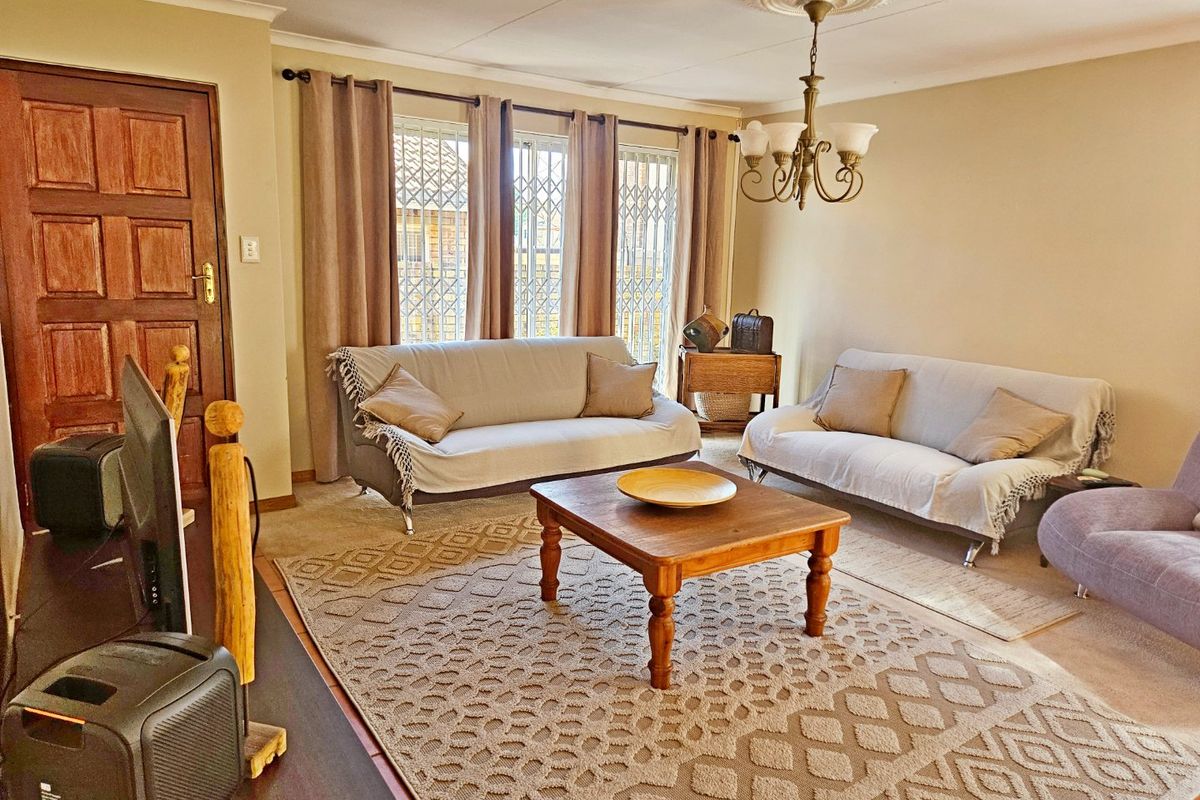 A comfortable living room featuring a decorative ceiling rose, classic chandelier, and secure window gates, providing a functional and well-lit space.