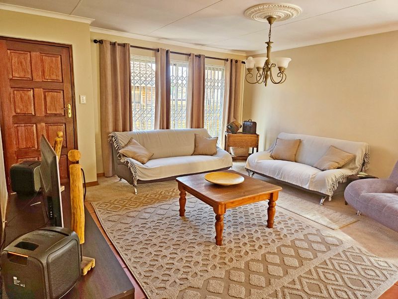 A comfortable living room featuring a decorative ceiling rose, classic chandelier, and secure window gates, providing a functional and well-lit space.