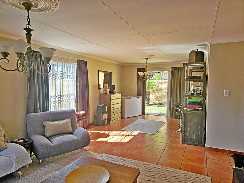 A living room featuring tiled flooring, ceiling roses, and a sliding glass door providing access to the rear garden area.