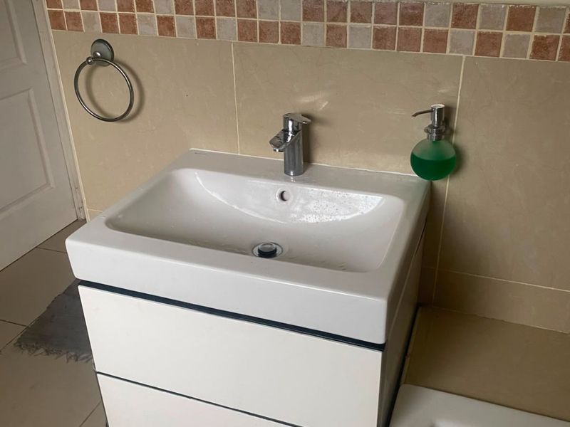 A functional bathroom featuring a modern white vanity cabinet with a ceramic basin, chrome mixer tap, and decorative tiled splashback.