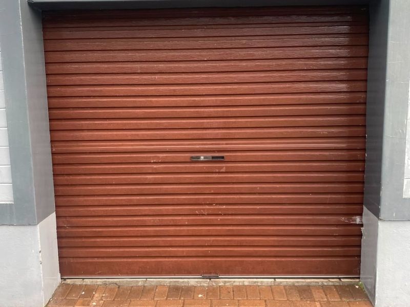 A secure, single-bay garage featuring a brown roller shutter door and paved driveway access.