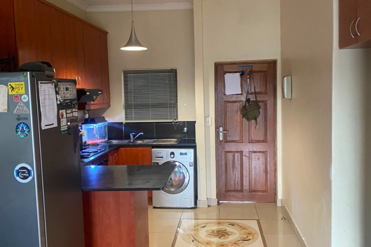 Functional kitchen featuring built-in wooden cabinetry, laminate countertops, tiled flooring with decorative inlay, and integrated plumbing for a washing machine.