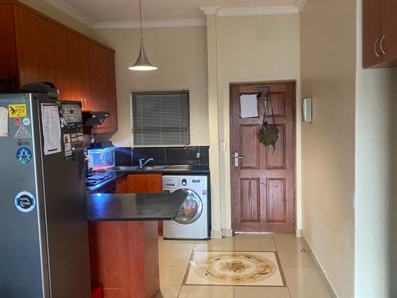 Functional kitchen featuring built-in wooden cabinetry, laminate countertops, tiled flooring with decorative inlay, and integrated plumbing for a washing machine.