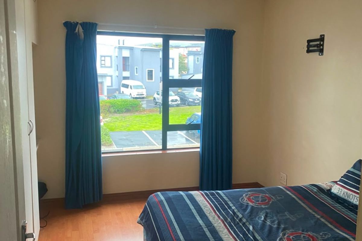 A functional bedroom featuring laminate flooring, a built-in wardrobe, and a window with views of the complex parking area.
