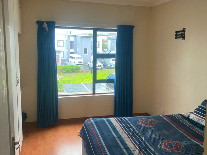 A functional bedroom featuring laminate flooring, a built-in wardrobe, and a window with views of the complex parking area.