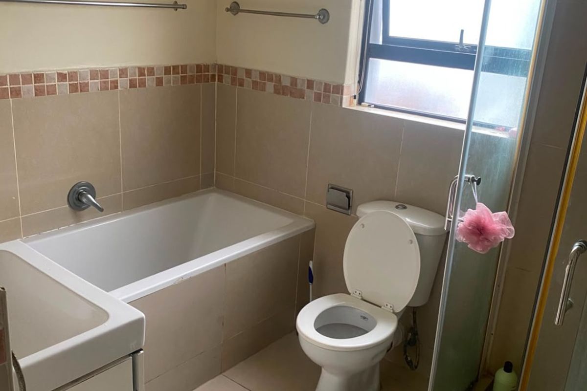 A functional bathroom featuring a built-in bathtub, separate shower enclosure, toilet, and vanity basin with neutral wall and floor tiling.