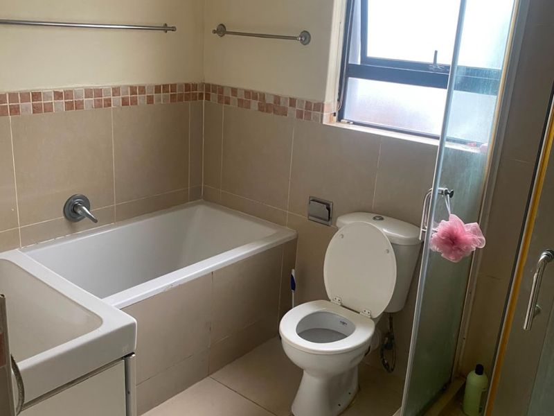 A functional bathroom featuring a built-in bathtub, separate shower enclosure, toilet, and vanity basin with neutral wall and floor tiling.