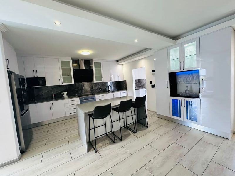 Modern kitchen featuring high-gloss white cabinetry, stone countertops, a central island with breakfast bar seating, and integrated display cabinets with accent lighting.