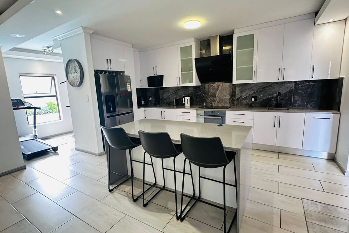 Modern kitchen featuring white cabinetry, dark marble-style backsplash, quartz-topped island, and integrated appliances, seamlessly flowing into an adjacent living area.