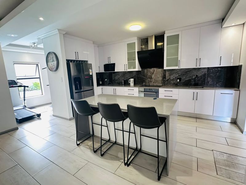 Modern kitchen featuring white cabinetry, dark marble-style backsplash, quartz-topped island, and integrated appliances, seamlessly flowing into an adjacent living area.