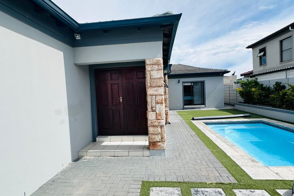 Rear exterior view featuring a paved patio area, swimming pool, artificial lawn, and a stone-clad pillar entrance to the home.