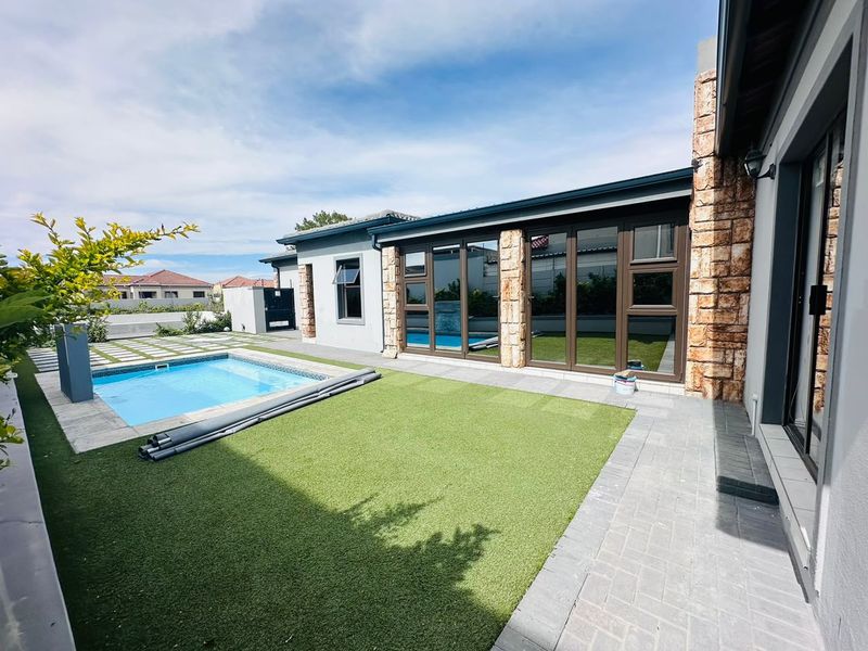 A well-maintained rear garden featuring a swimming pool, artificial lawn, paved patio area, and modern aluminium stacker doors leading into the home.