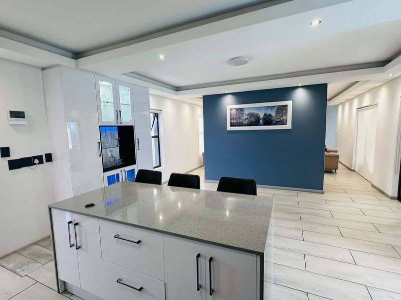 Modern kitchen featuring a central island with stone countertops, sleek white cabinetry, recessed lighting, and contemporary tiled flooring in an open-plan layout.