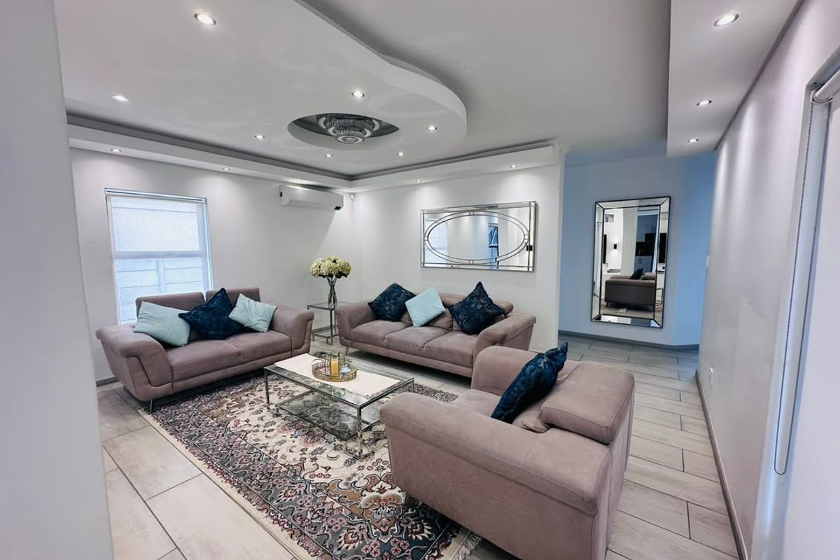 A modern, well-maintained living room featuring a decorative recessed ceiling with integrated downlights, tiled flooring, and a wall-mounted air conditioning unit.