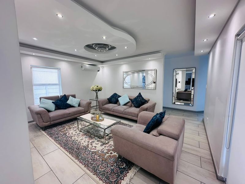 A modern, well-maintained living room featuring a decorative recessed ceiling with integrated downlights, tiled flooring, and a wall-mounted air conditioning unit.