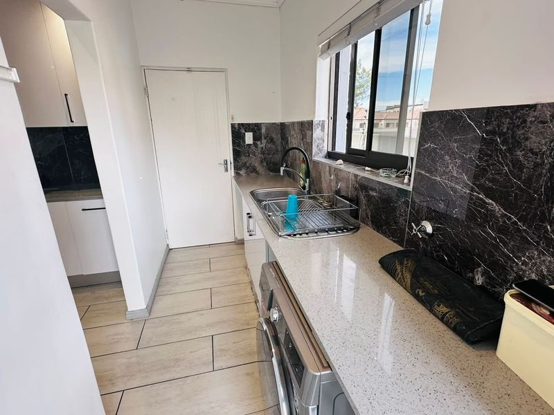 A functional laundry room featuring stone countertops, a stainless steel sink, marble-look splashbacks, and tiled flooring with built-in cabinetry.