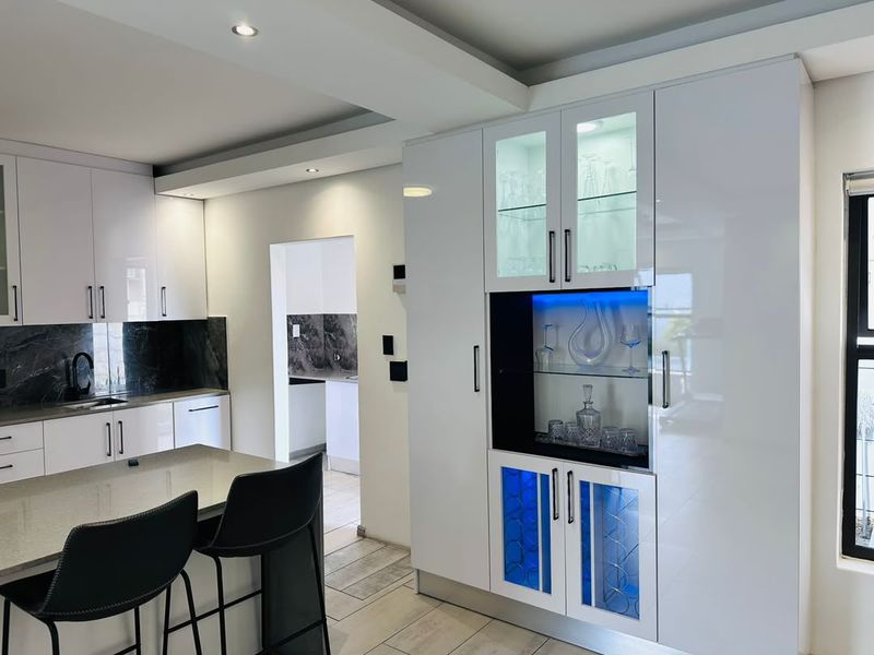 Modern kitchen featuring high-gloss white cabinetry, stone countertops, marble-look splashback, and a custom integrated display unit with ambient LED lighting.