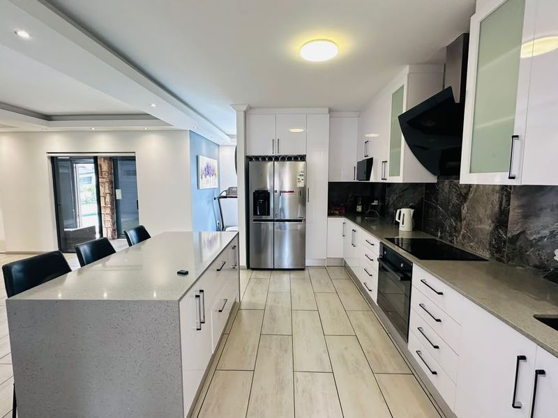 Modern kitchen featuring a large central island, sleek white gloss cabinetry, quartz countertops, integrated appliances, and contemporary tiled flooring.