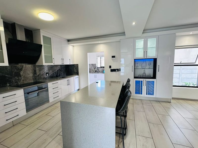 Modern kitchen featuring white cabinetry, quartz countertops, a central island, built-in appliances, and stylish stone splashbacks with integrated display lighting.
