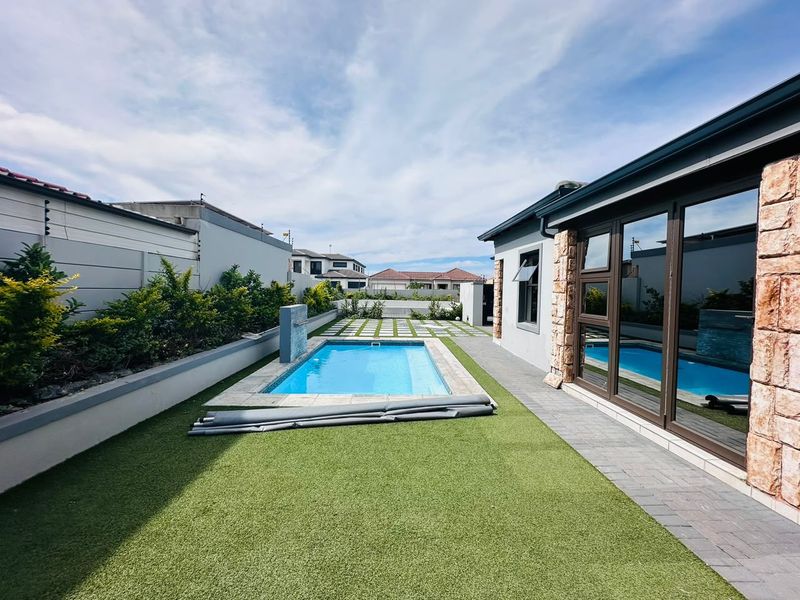 A well-maintained rear garden featuring a swimming pool, artificial lawn, paved patio area, and modern stone-clad exterior wall finishes.