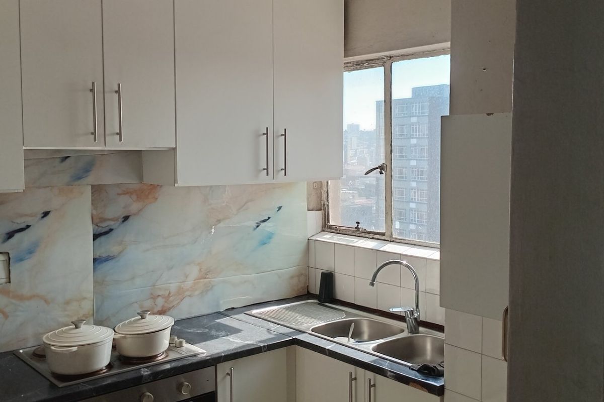 Compact kitchen featuring white cabinetry, marble-effect splashback, stainless steel sink, and built-in oven with electric hob, offering functional workspace with city views.