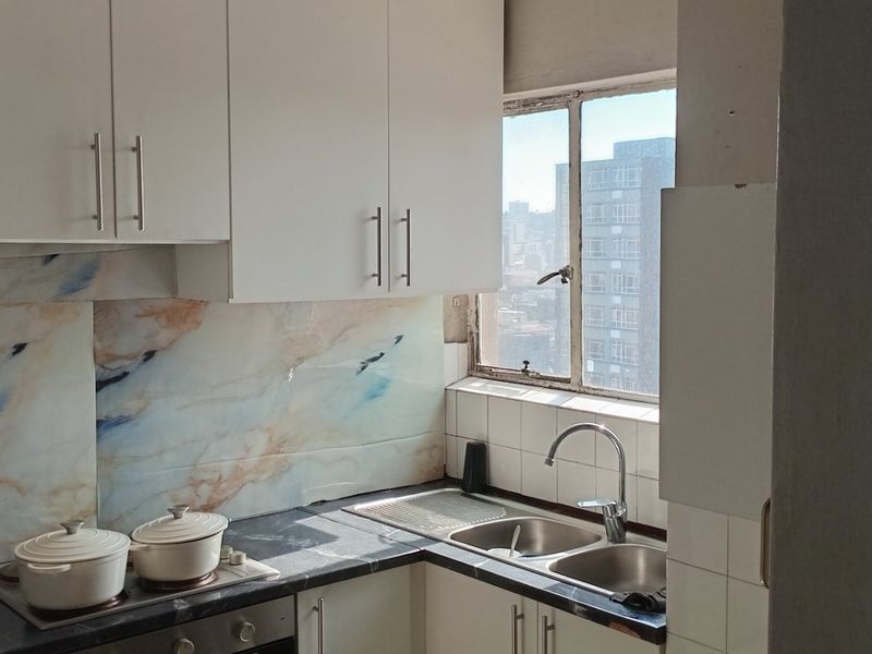 Compact kitchen featuring white cabinetry, marble-effect splashback, stainless steel sink, and built-in oven with electric hob, offering functional workspace with city views.