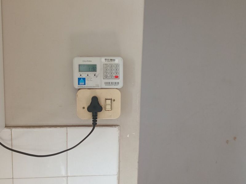 A close-up view of a wall-mounted prepaid electricity meter and electrical outlet with tiled splashback.