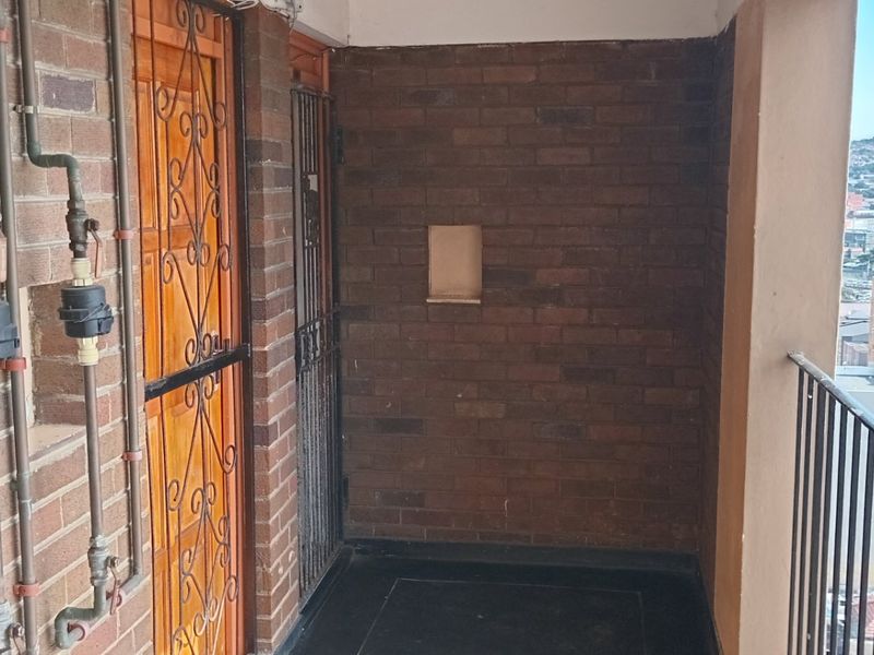 A functional balcony area featuring exposed brick walls, metal security gates, and an open view of the surrounding urban landscape.