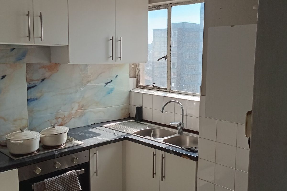 Compact kitchen featuring white cabinetry, marble-effect splashback, built-in oven and hob, and a double sink with a window view.