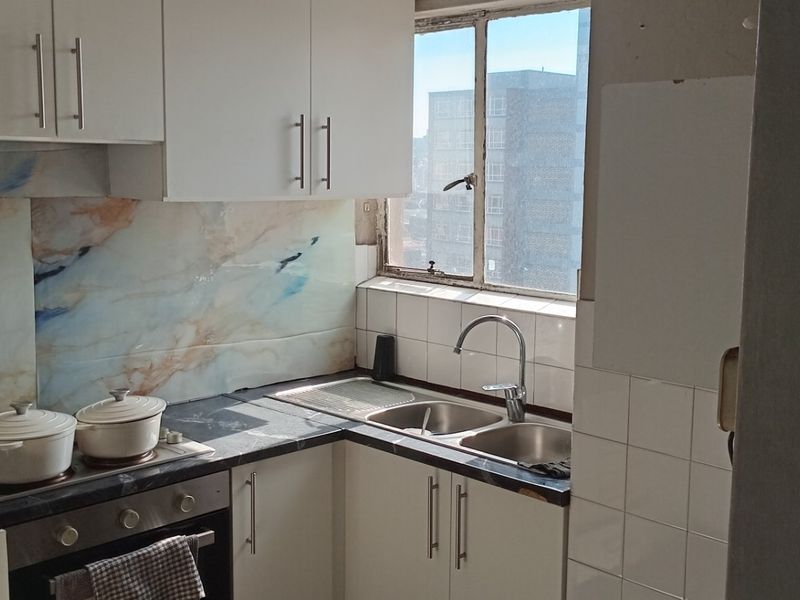 Compact kitchen featuring white cabinetry, marble-effect splashback, built-in oven and hob, and a double sink with a window view.