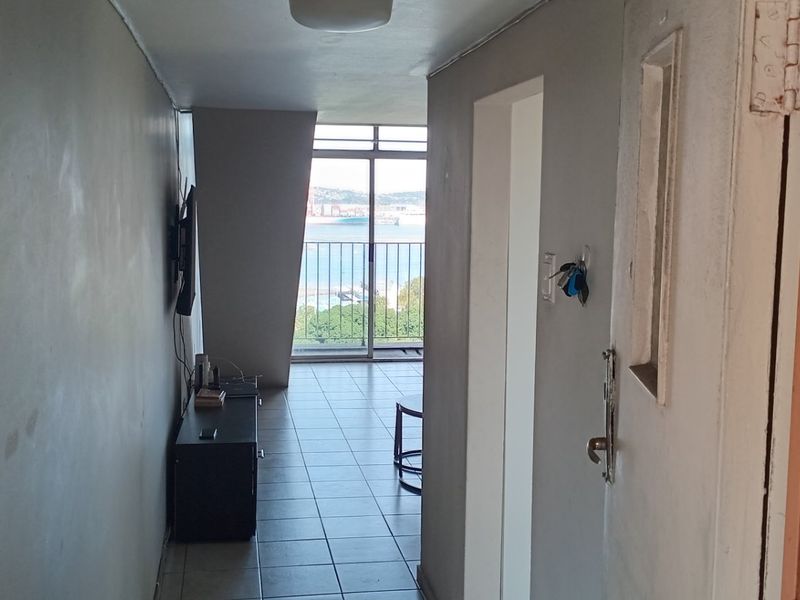 Entryway leading into an open-plan living area with tiled flooring and a sliding glass door providing access to a balcony with coastal views.