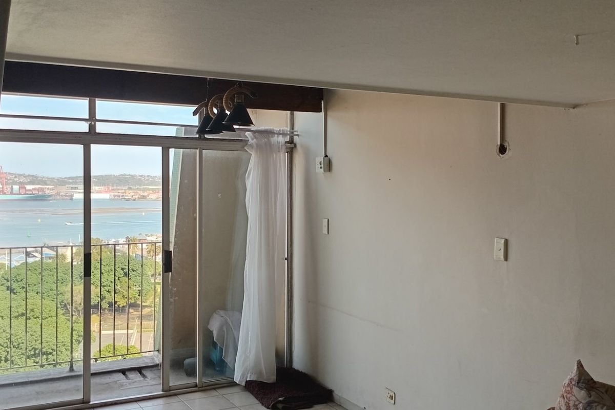 An empty living room featuring a large sliding glass door with access to a balcony and views of the harbor.