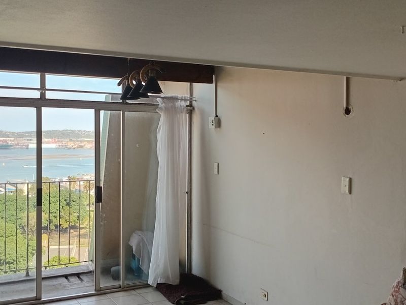 An empty living room featuring a large sliding glass door with access to a balcony and views of the harbor.