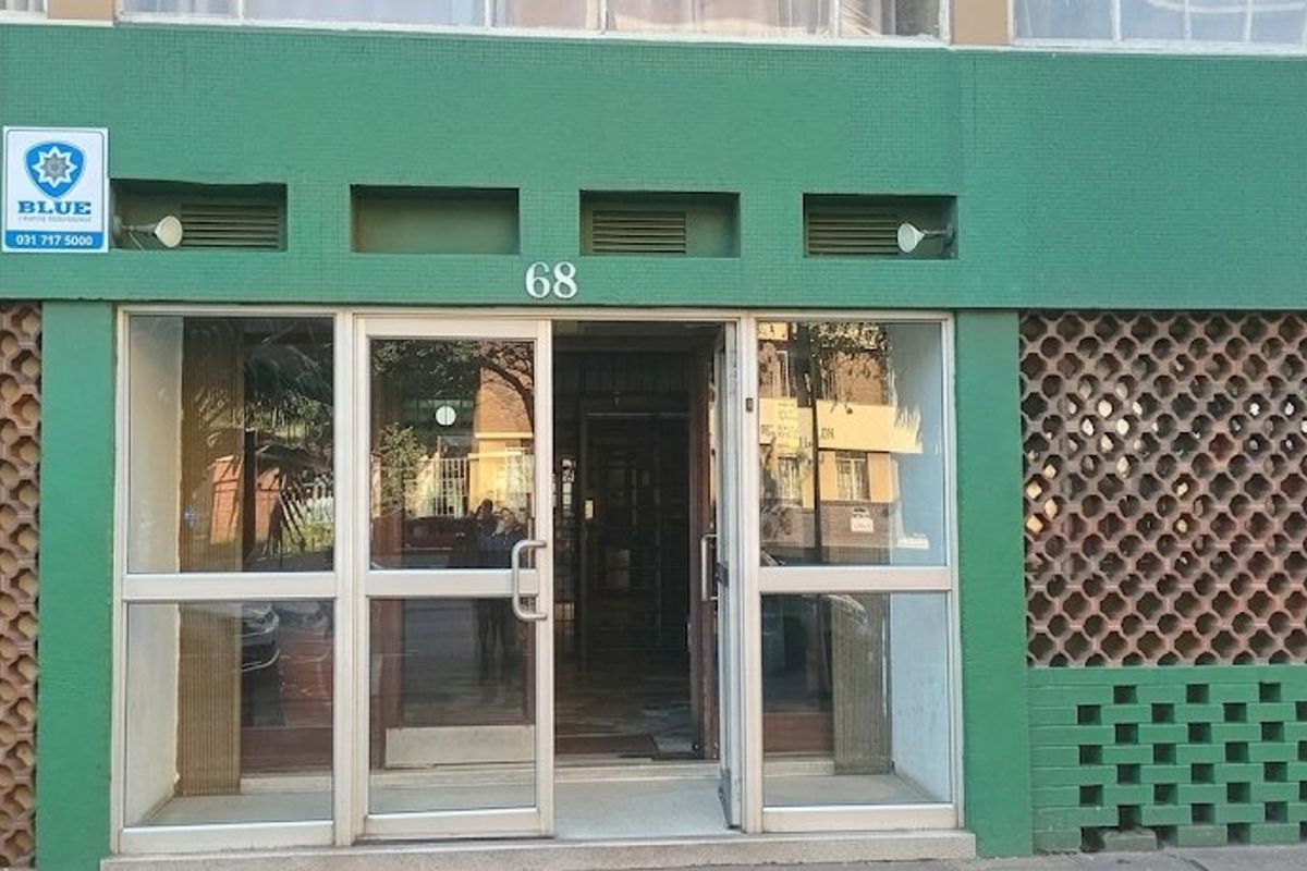 The front entrance of the apartment building features a glass door with aluminium framing and decorative breeze block wall detailing.