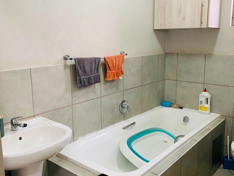A functional bathroom featuring a pedestal basin, a tiled built-in bathtub, and overhead cabinetry, offering a practical layout with neutral finishes.