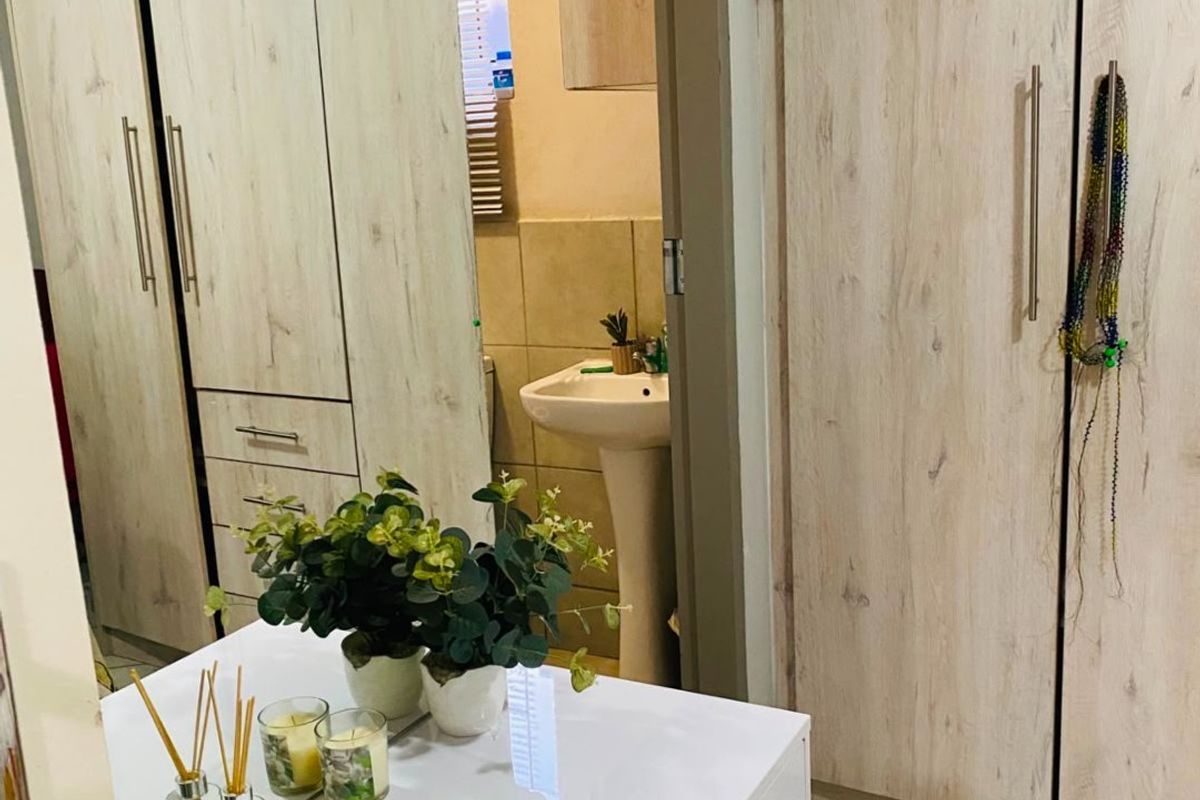 Bedroom featuring light wood-finish built-in cupboards and tiled flooring, with a view into an adjoining bathroom area with a pedestal basin.