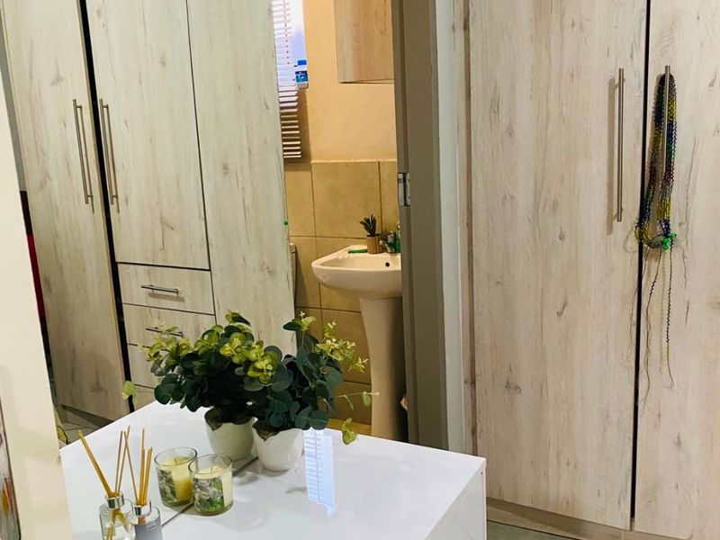 Bedroom featuring light wood-finish built-in cupboards and tiled flooring, with a view into an adjoining bathroom area with a pedestal basin.