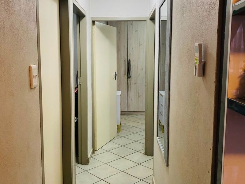 A functional hallway featuring tiled flooring, neutral wall finishes, and access to multiple rooms with built-in storage visible at the end.