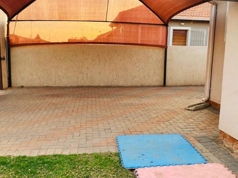 Outdoor patio area featuring paved flooring, a large shade sail structure, and a wall-mounted air conditioning unit.